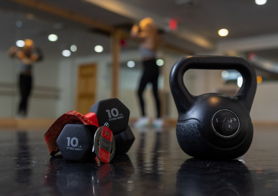 Kettlebell and dumbbells on the studio floor with Lisa training in the background